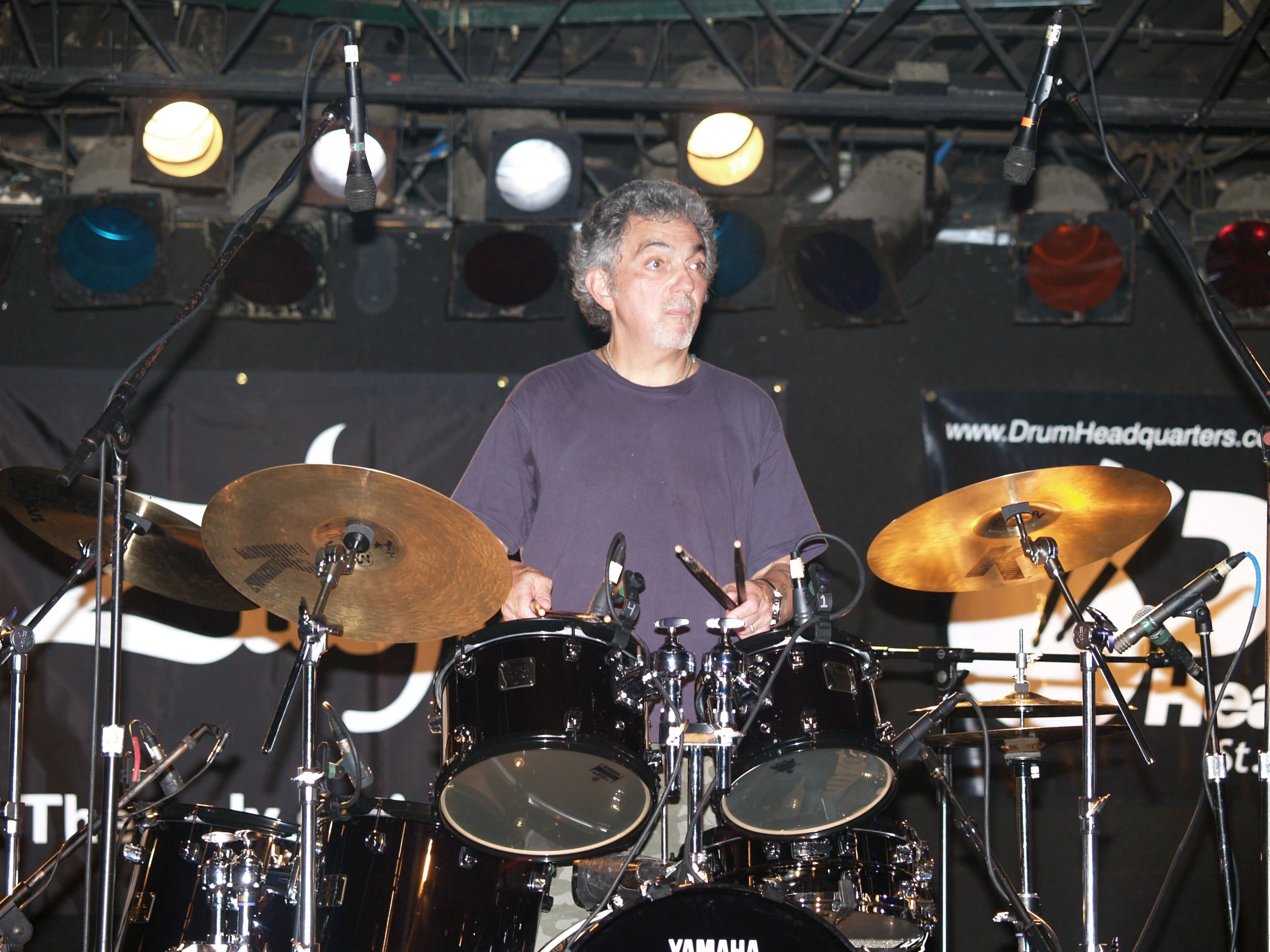 a man on stage with drums, holding it up to the drum sticks