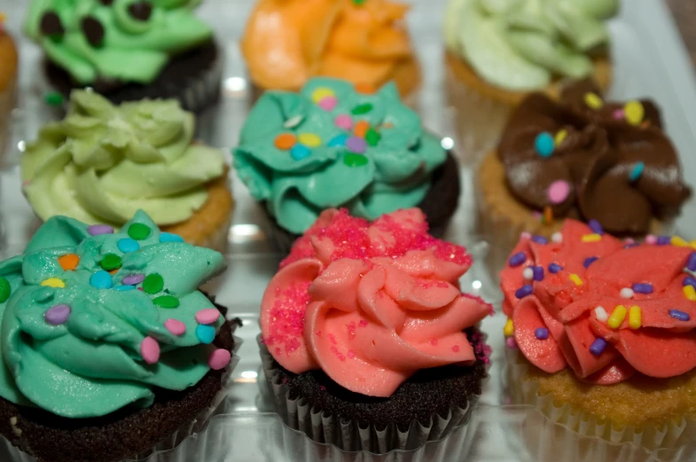 a box of colorful frosted cupcakes that are in plastic containers