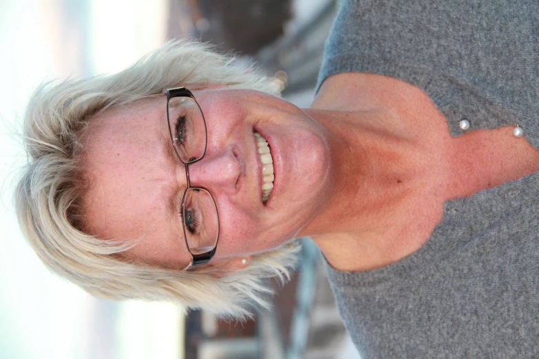 a woman wearing glasses and grey shirt smiling for the camera