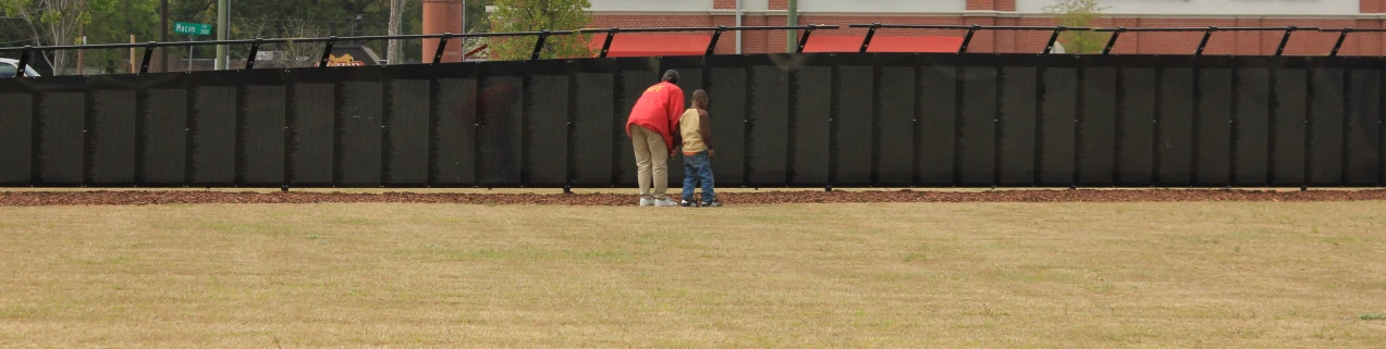 a man in blue jeans with red vest standing by fence