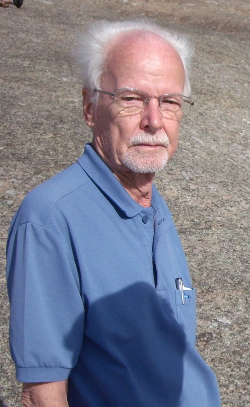 an older man with glasses and white hair is standing in the middle of a lot