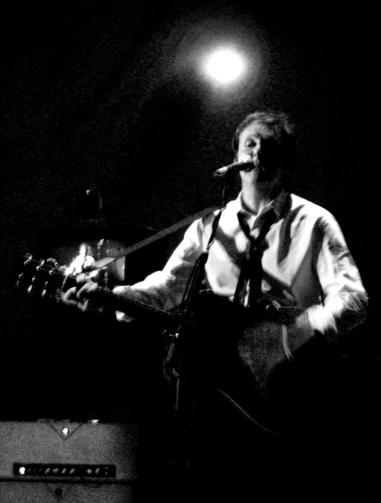 a man in white shirt and tie singing into microphone