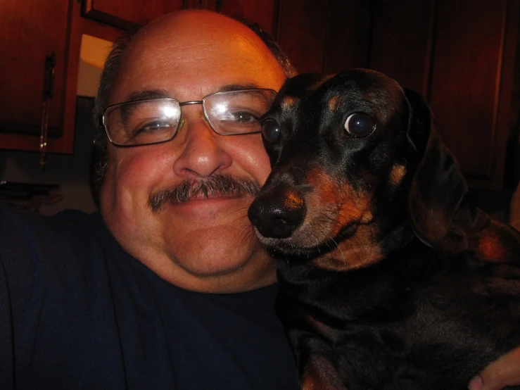 a man smiles with his dog while wearing glasses