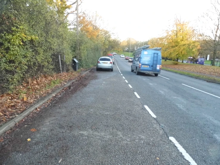 several cars driving down a long street with trees lining the sides