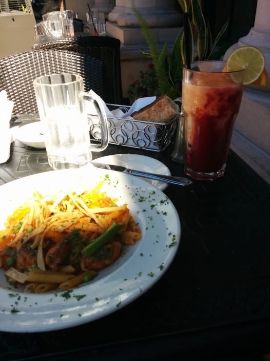 a plate with pasta, vegetables, and a drink on the table