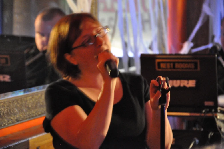 a woman talking on a microphone while someone else is playing guitar