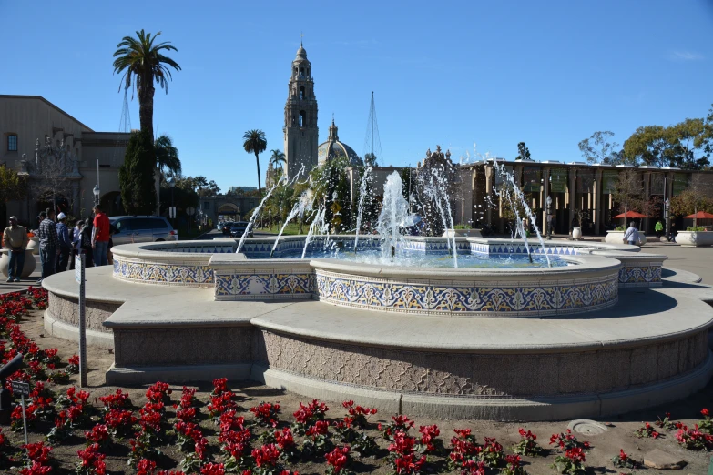 a fountain near some palm trees with buildings in the background