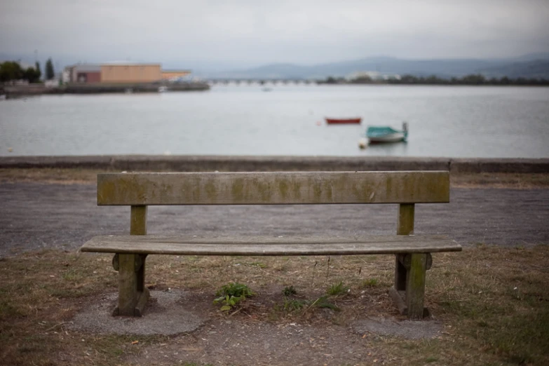 a wooden park bench sitting next to a lake with a boat in the water