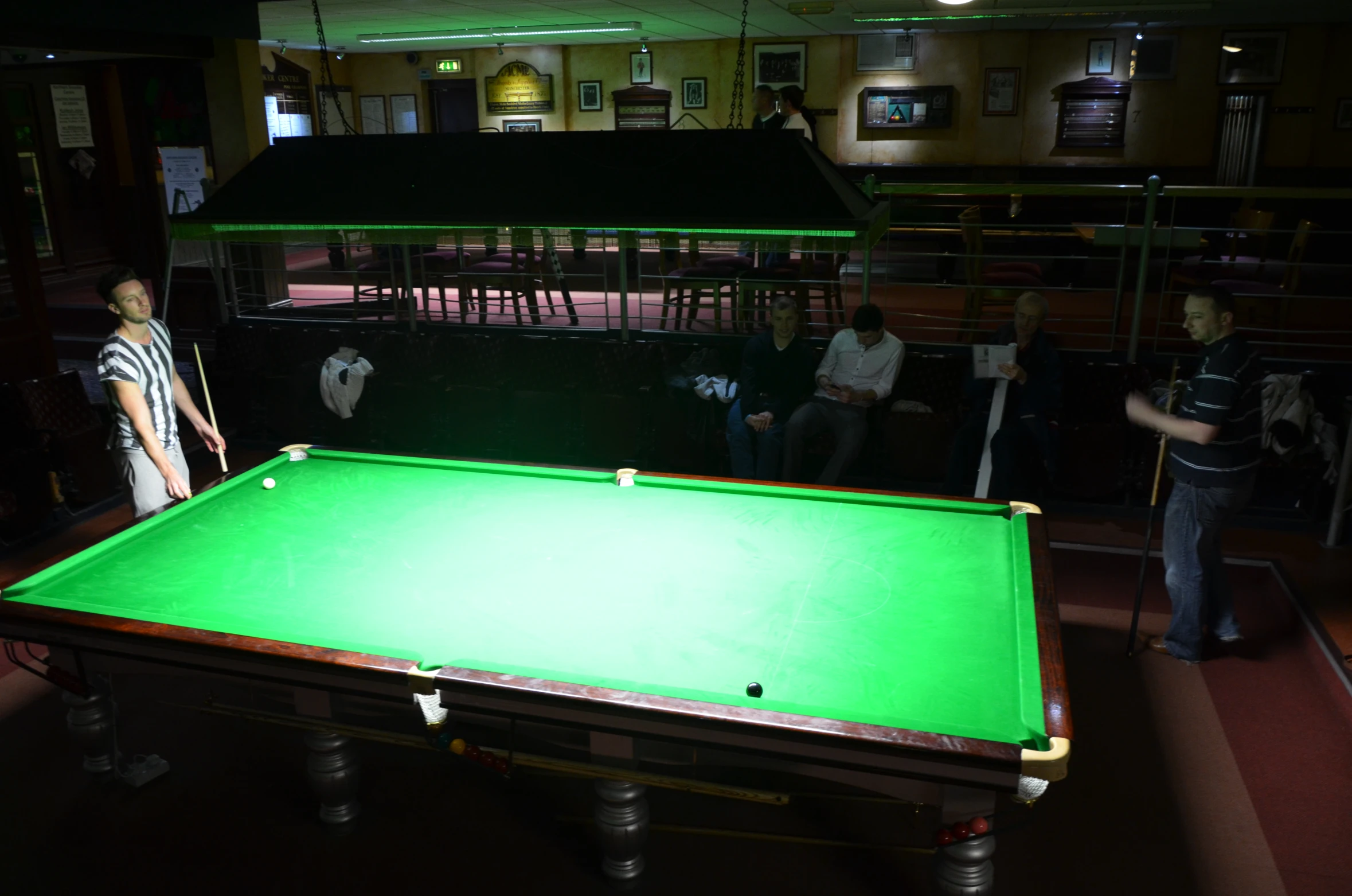 two people are playing pool in a dark bar