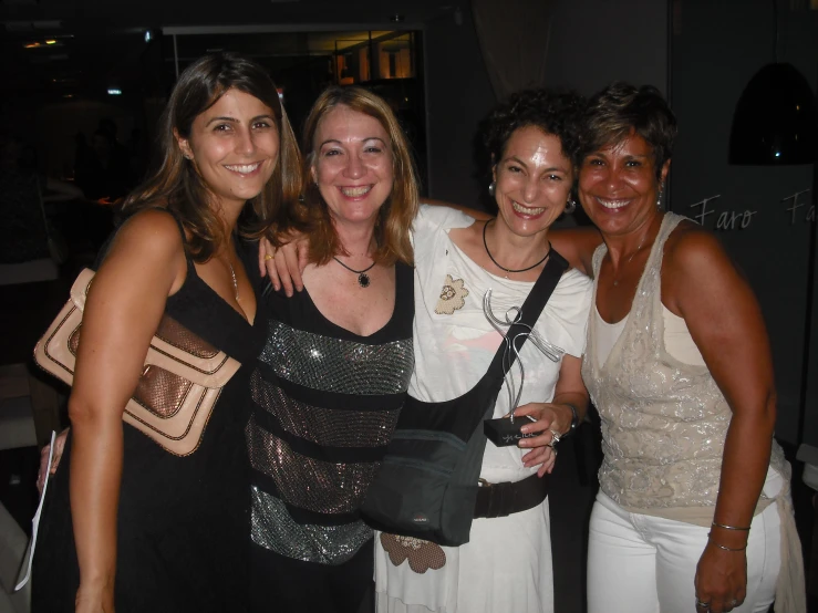 four women posing for the camera with a large purse on one shoulder