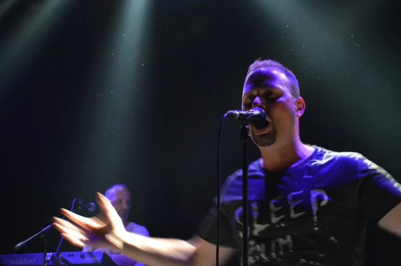 a man singing into microphones on a stage