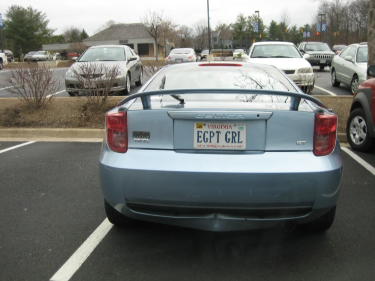 the back of a blue car in a parking lot with several parked vehicles