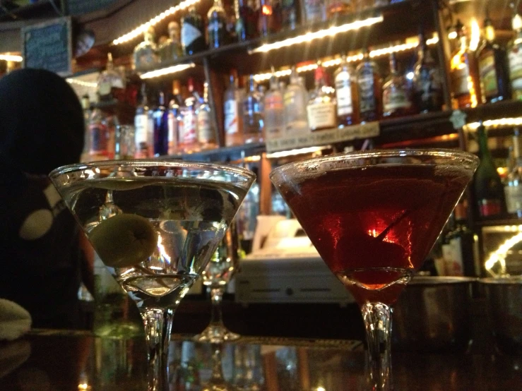two alcoholic drinks in martini glasses are at a bar