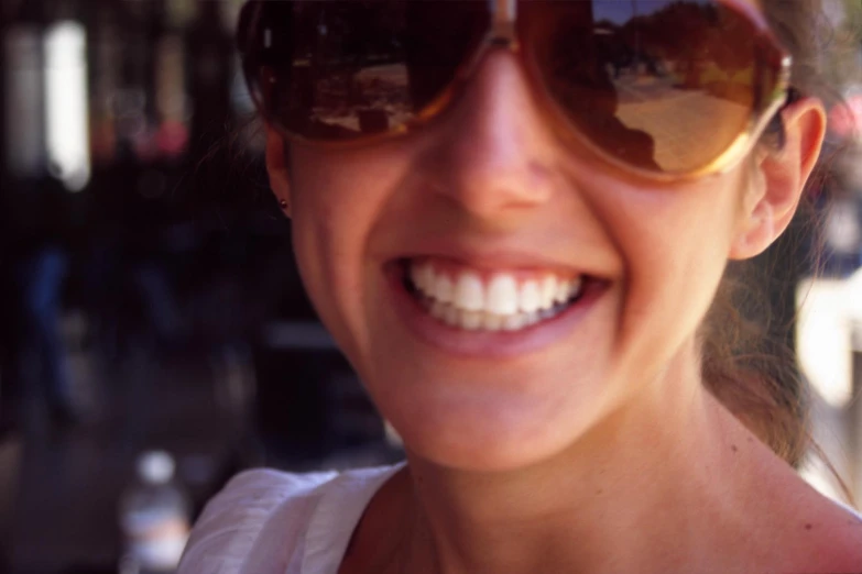 a woman smiling and wearing sunglasses with a big smile