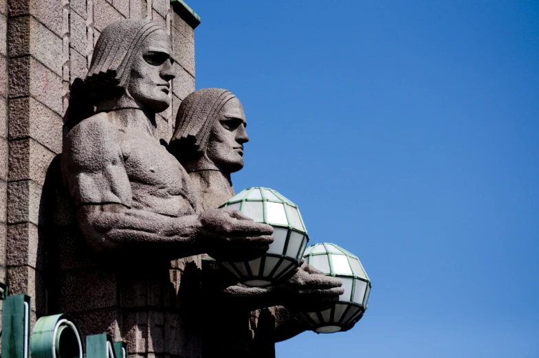 two statues of man holding an orb next to a brick building