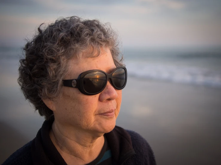 an old woman wearing sunglasses while standing near the water