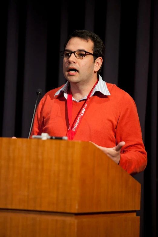 a man wearing glasses speaks from behind a podium