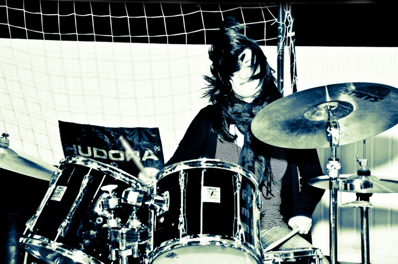 a person with long hair plays drums behind a volleyball net