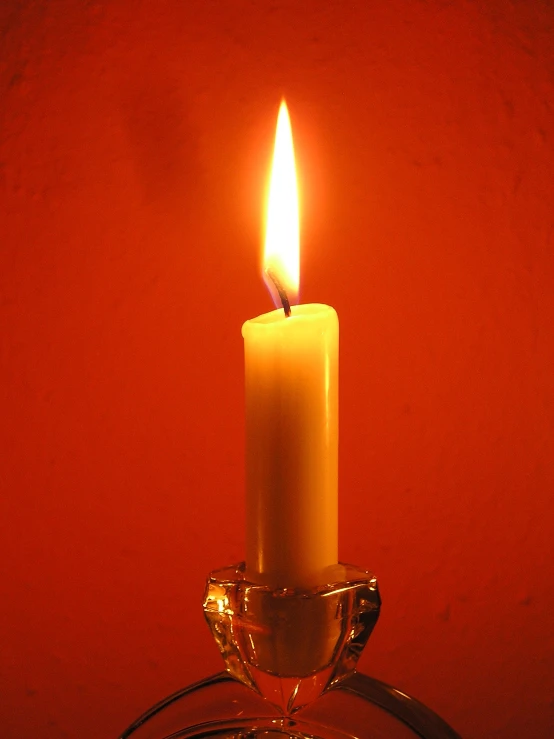 a single candle burning next to a wire on a red background