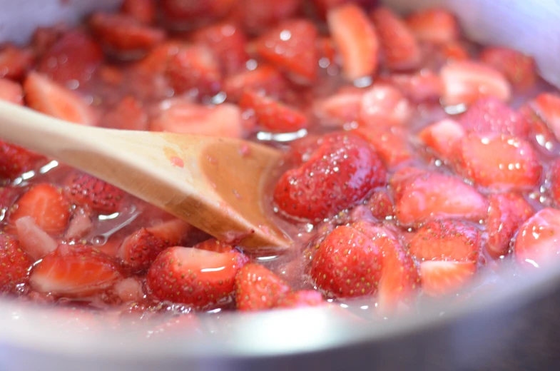 a pot filled with strawberries and a wooden spoon