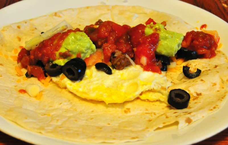 a burrito is on a plate topped with eggs, sauce and avocado
