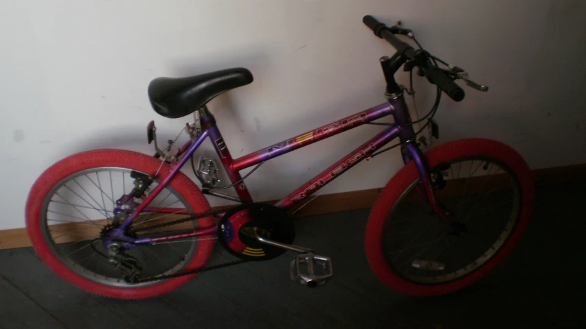 a purple and red bike leaning on the wall