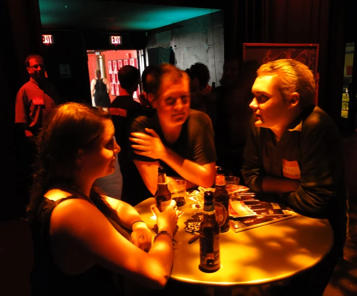 two men and a woman seated around a table in a dark room