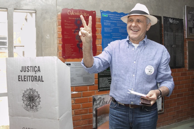 a man with a hat on holding his fingers up