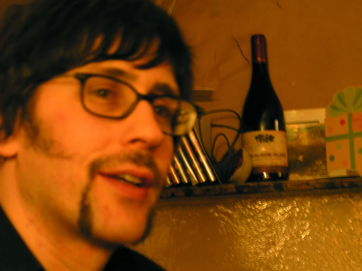 a man with glasses next to a glass bottle of wine