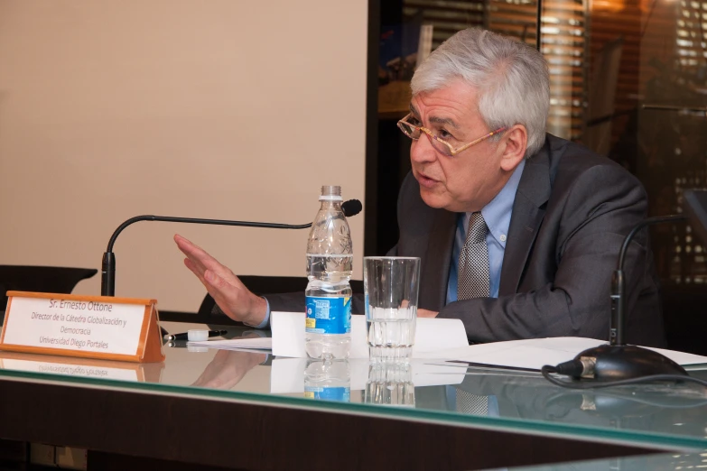 a man sitting at a table with a water bottle and a wooden sign