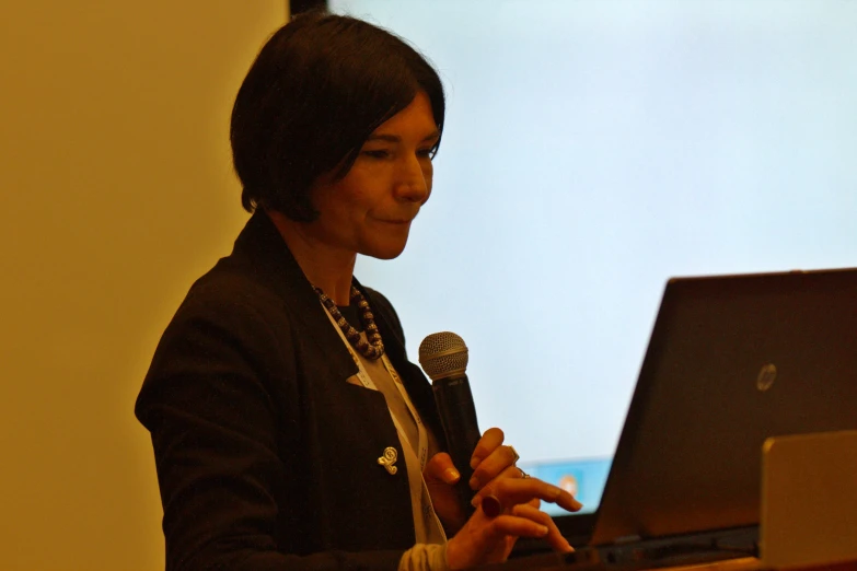 a woman speaking into a microphone in front of a laptop computer