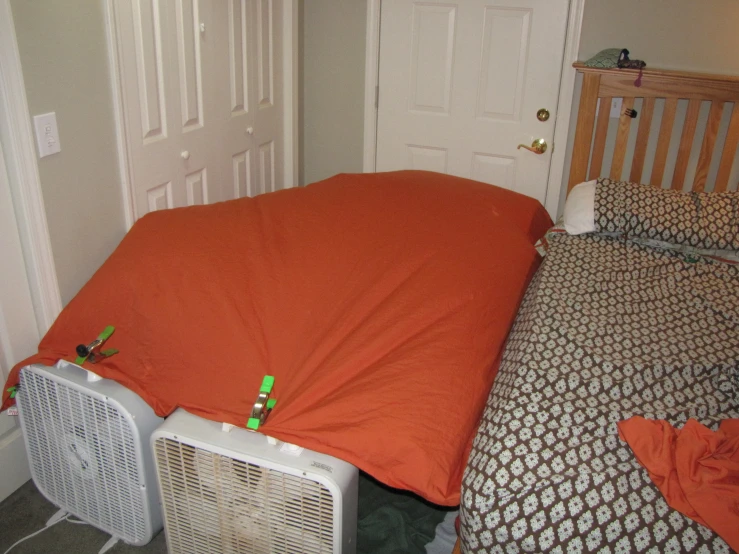 an orange sheet is on top of the bed and two small white speakers are below it