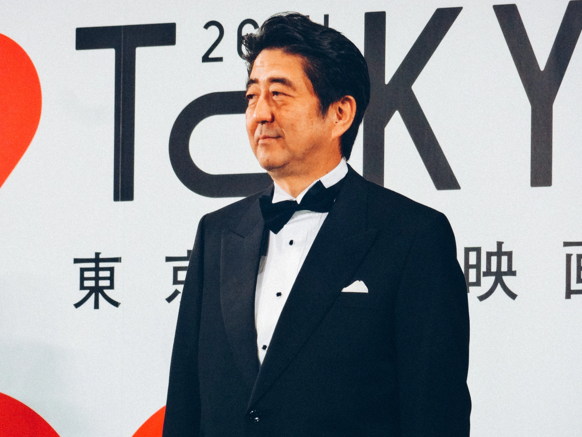 japanese man in a tuxedo stands with one hand in his pockets