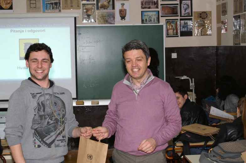 two men in grey sweaters holding brown bags