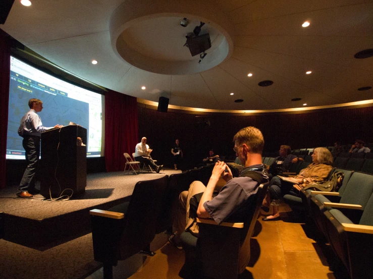 people sitting in chairs around a table and listening to a speaker