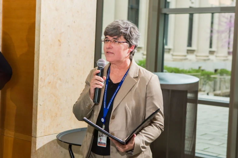 a woman speaking into a microphone in front of a window