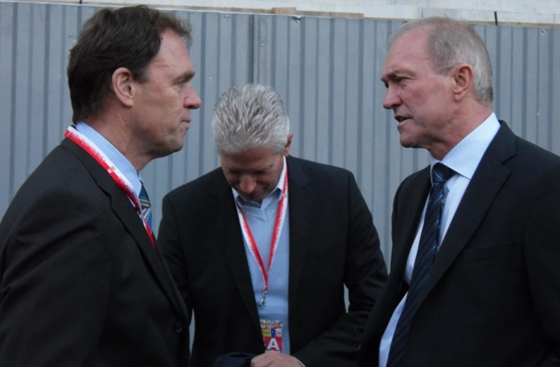 three men standing close to each other wearing suits