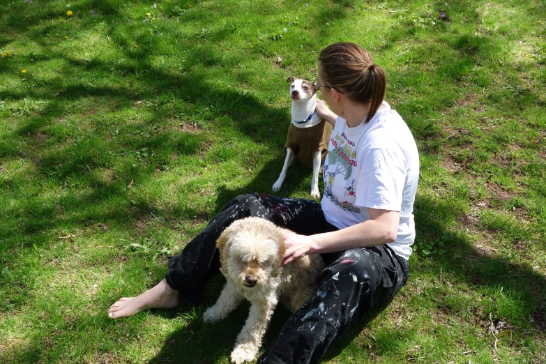 the woman is sitting on the grass playing with her dog