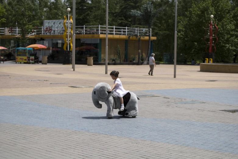 a man riding an elephant toy in the middle of a courtyard