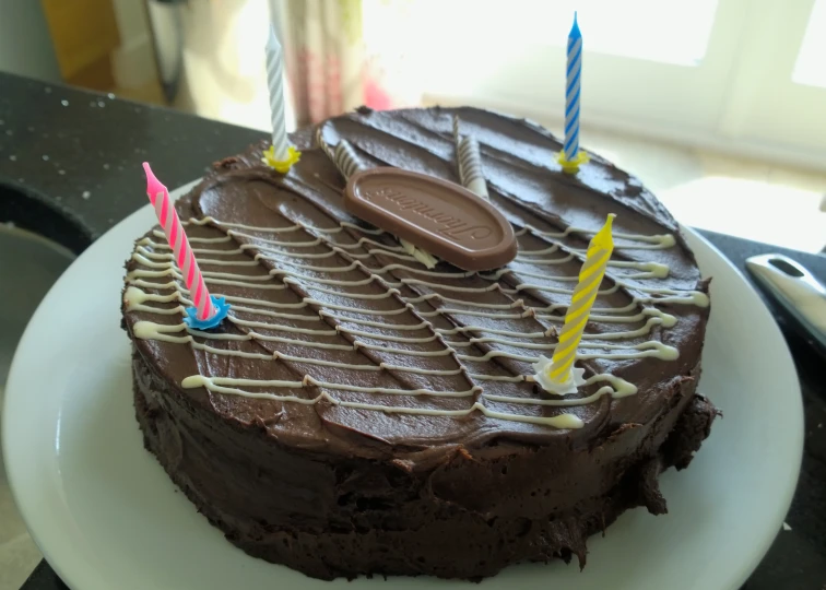 a chocolate birthday cake with lit candles sits on a white plate