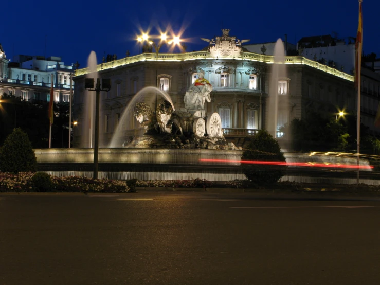 an illuminated fountain with buildings behind it