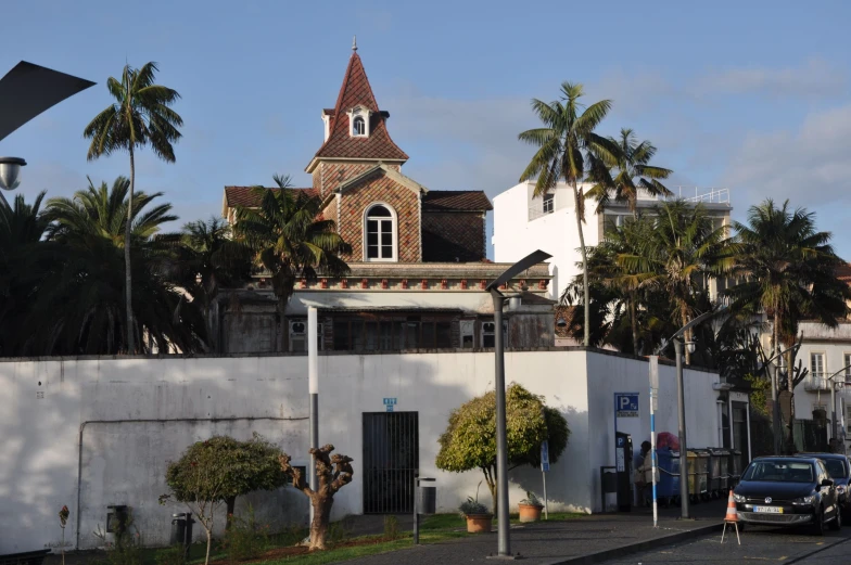 an old, wooden building with a steeple stands on a street corner in front of palm trees