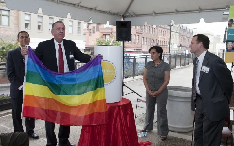 a group of people stand around a rainbow flag