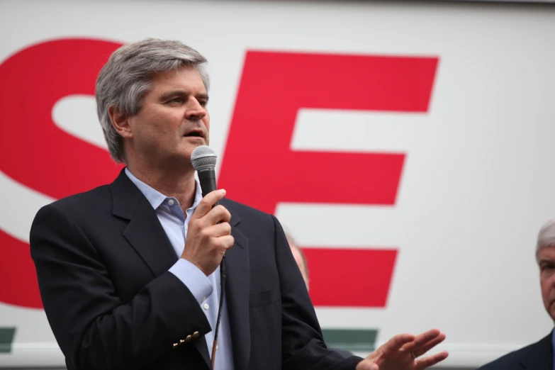 an old man in business attire holding a microphone