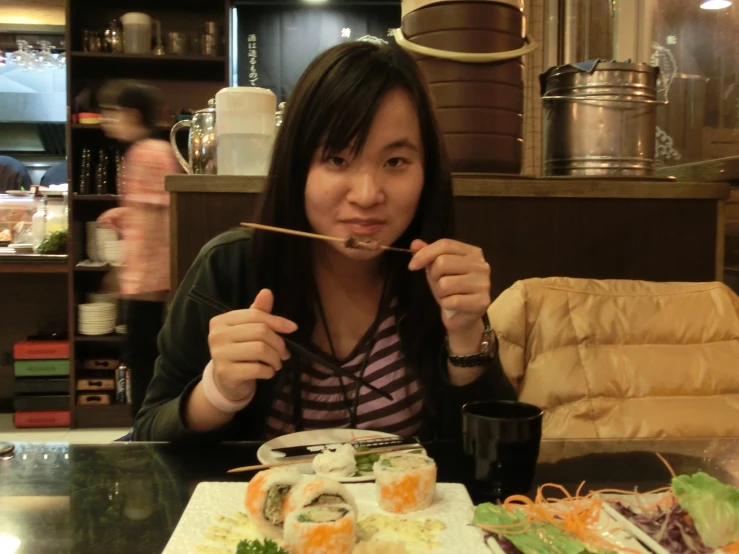 a woman in striped shirt sitting at table with sushi