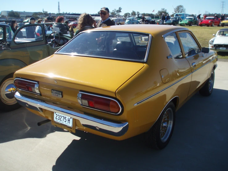 a yellow vintage car sits parked in a lot next to other cars