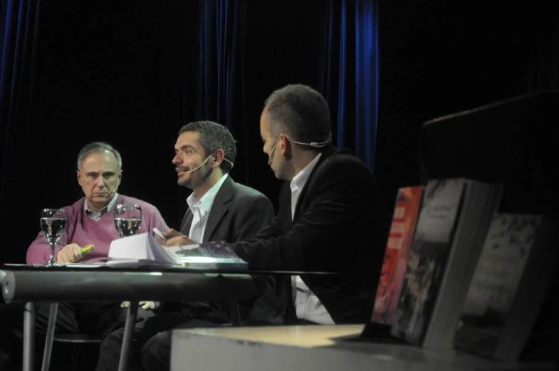 three men sitting at a table with books