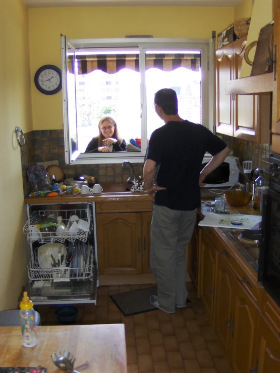 a man looking out the window as a woman opens up the dishwasher