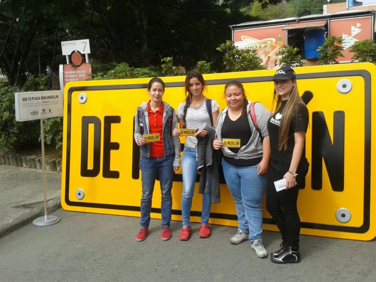 three girls are standing against a street sign