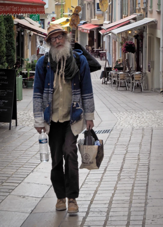 an older man with a long beard carries two shopping bags